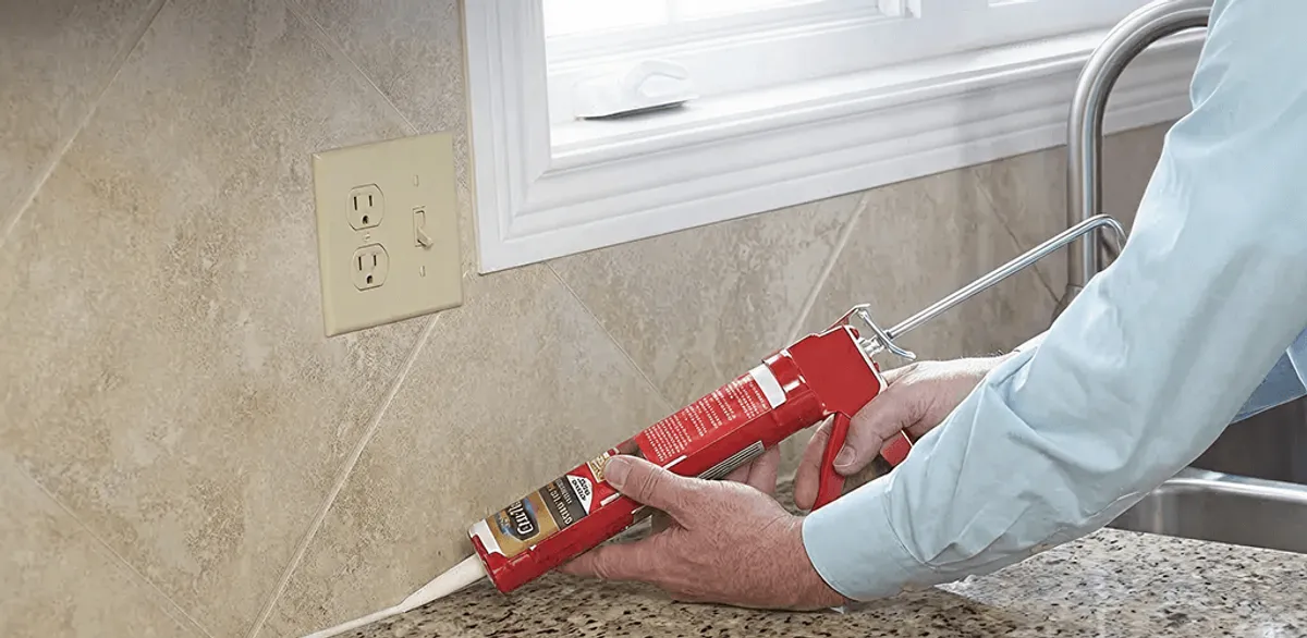 Handyman applying caulk along a kitchen backsplash and countertop seam in Grand Rapids, MI