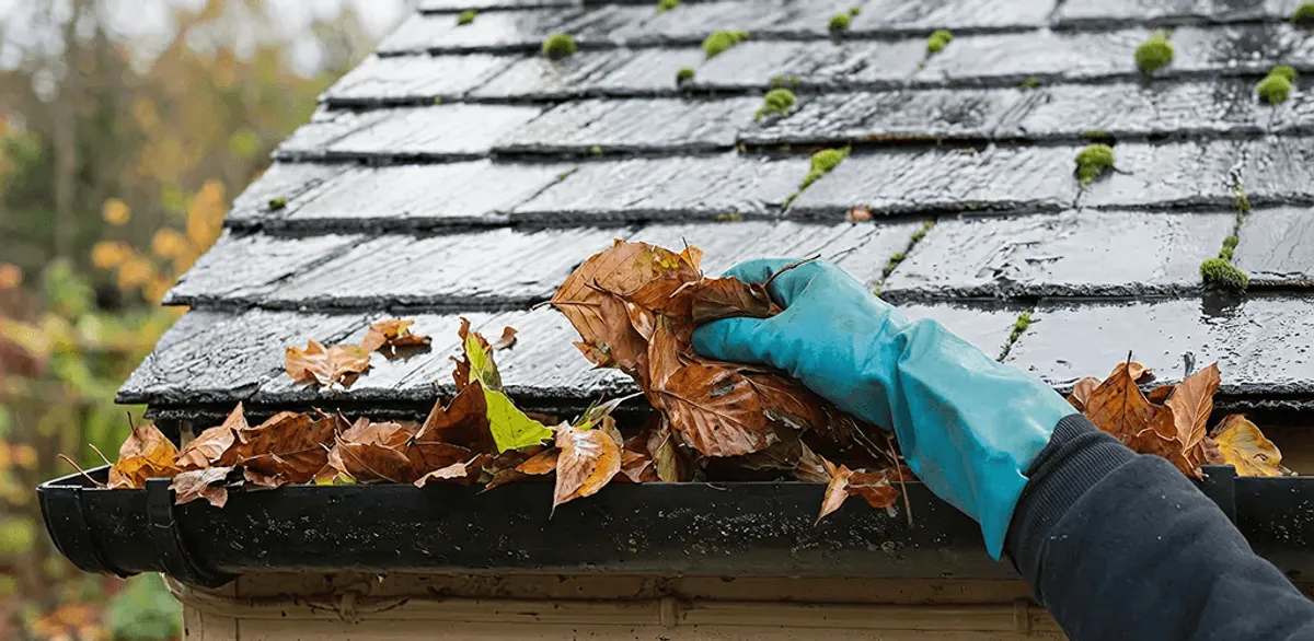 Gutter cleaning technician clearing wet leaves from roof gutters in Grand Rapids, MI